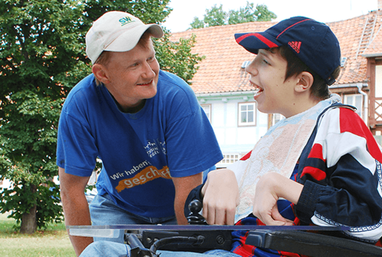 Freiwilliger Helfer unterhält sich mit einem behinderten Jungen im Rollstuhl.