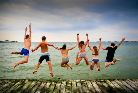 Menschengruppe in Badekleidung springt in einen See im Sommer