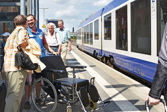 Ehrenamtlicher Mitarbeiter der ökumenischen Bahnhofmission hilft Zugreisende mit dem Rollstuhl.