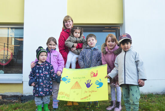 Gruppe von Kita-Kindern und eine Erzieherin stehen mit einem Plakat vor einem Gebäude
