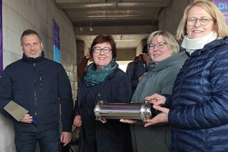 Gruppe von Personen in einem Gang, eine Person hält einen zylindrischen Metallbehälter